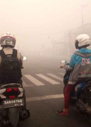 Foto dua pengendara sepeda motor berhenti di lampu merah Jalan Tjilik Riwut Palangka Raya di tengah kabut asap tebal akibat karhutla.