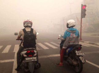 Foto dua pengendara sepeda motor berhenti di lampu merah Jalan Tjilik Riwut Palangka Raya di tengah kabut asap tebal akibat karhutla.