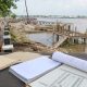 Ilustrasi proyek Waterfront City Kapuas dengan area tepi sungai, dermaga belum selesai, dan dokumen perencanaan pembangunan.