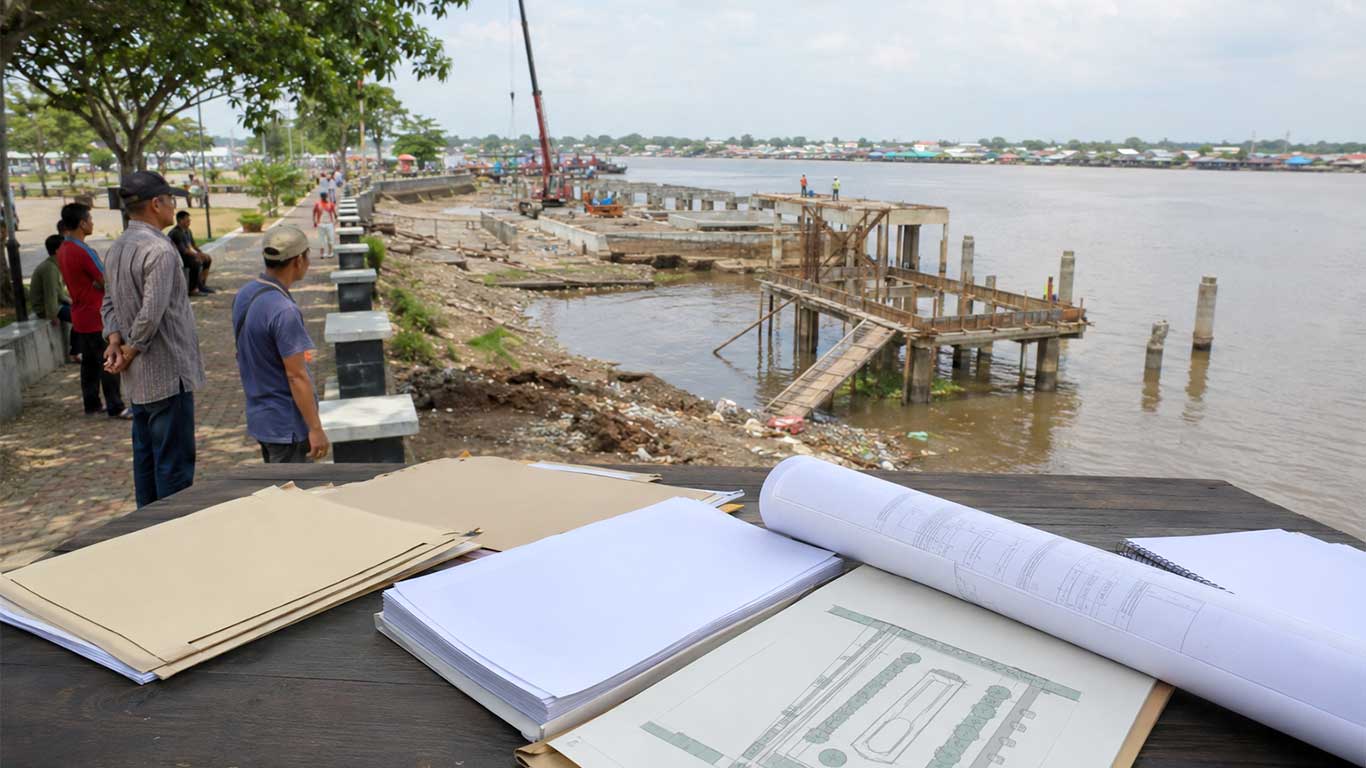 Ilustrasi proyek Waterfront City Kapuas dengan area tepi sungai, dermaga belum selesai, dan dokumen perencanaan pembangunan.